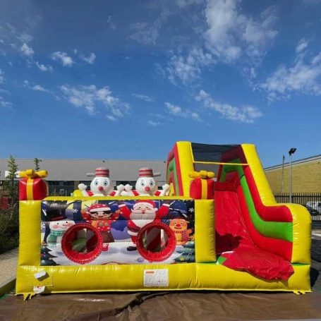 Château gonflable coloré avec toboggan et motifs de Noël.